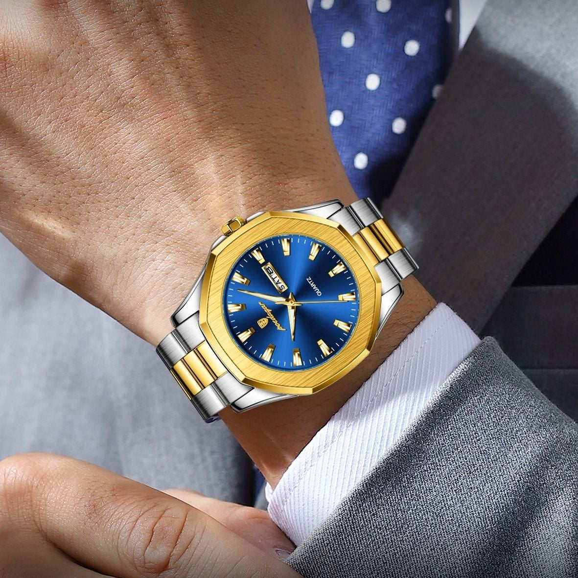 Gold and silver watch with blue face on a wrist, wearing a suit and tie.